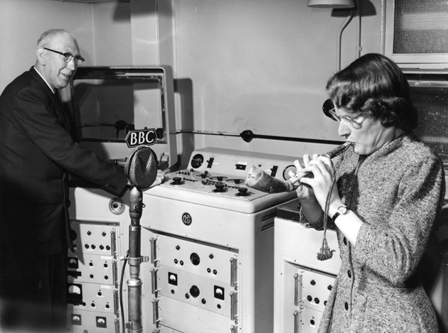 Daphne oram blowing a Mijwiz, an Arabic reed pipe, while Richard Bird records the sound on a tape machine. BBC Radiophonic Workshop, Maida Vale, 1958