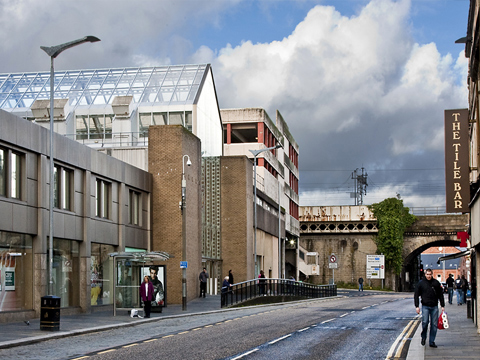 View along Smithhills Street in Paisley, showing the back of a late 20th Century shopping centre with a raised railway line behind..