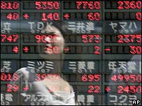 Mulher passa por painel com indicadores financeiros em Tóquio