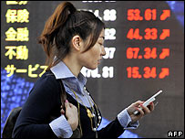 Một phụ nữ bước qua bảng giá cổ phiếu tại Tokyo