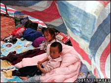 Hai em nhỏ ngồi dưới mái lều nylon on tạm bợ