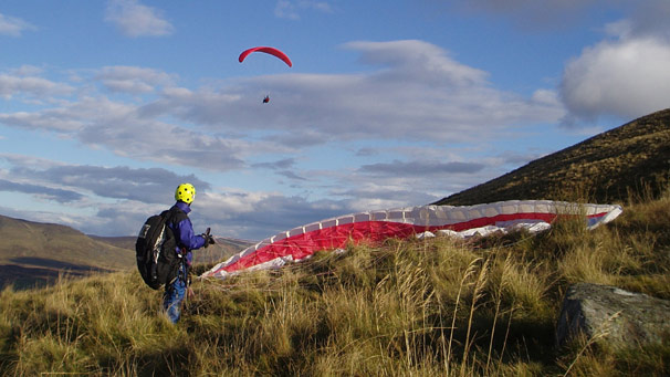 One airborne paraglider and one on a hillside