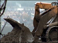 Digger at waste tip with houses in the background