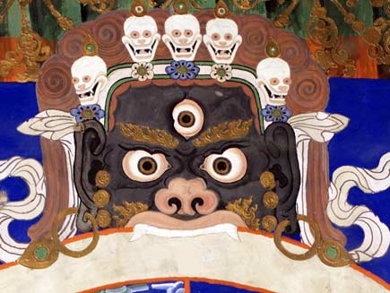 Black-skinned monster with flames playing over his eyebrows and licking from his open mouth. He is sinking his fangs into the wheel of the universe. He has three fierce eyes and is wearing a crown of skulls