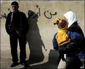 Palestinka s dítětem na cestě do volební místnosti míjí palestinského policistu, Abu Dis, západní břeh Jordánu