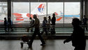 Passengers in a busy airport terminal, with planes in the background