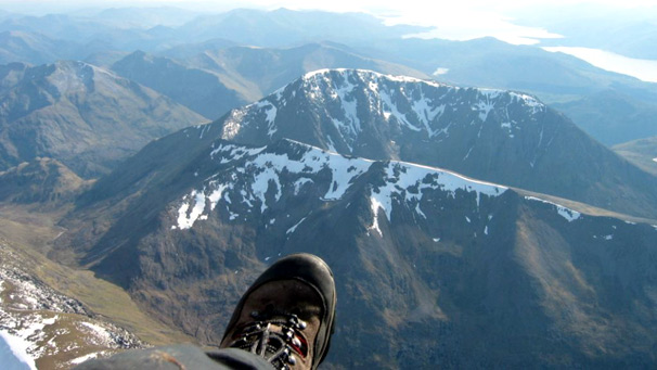 Paraglider's foot in foreground of aerial shot above snowy mountain