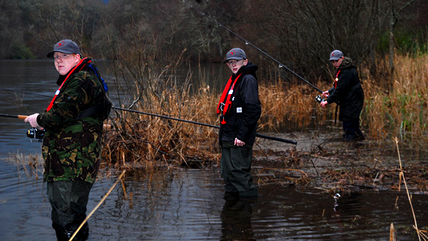 three boys fishing whilst knee deep in the river