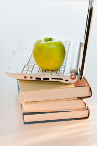 An apple on top of an computer resting on a pile of books.