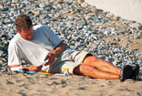 Dyn yn darllen ar y traeth © Bwrdd croeso Cymru