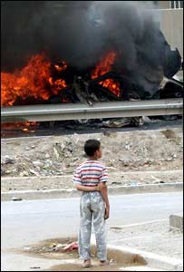 Menino iraquiano observa veículo militar dos EUA em chamas após atentado no bairro de Dura, em Bagdá