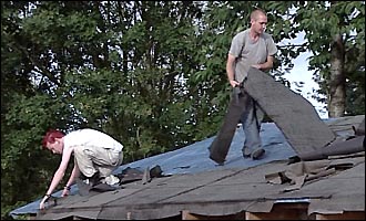 Two men strip off roofing material