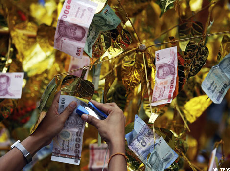 A person attaches a Thai banknote to an artificial tree
