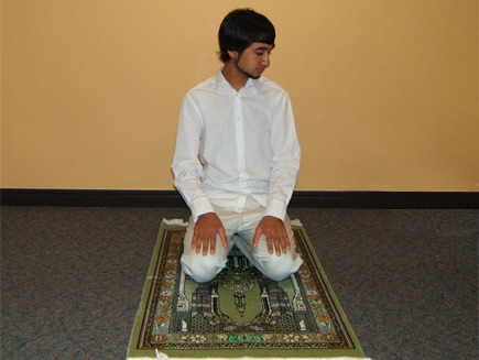 A man sits on his heels with his hands on his thighs, his head facing towards his left