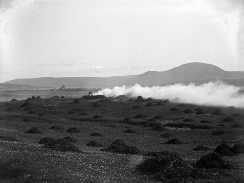 A figure tends to a smoking fire in a field covered with small heaps of seaweed