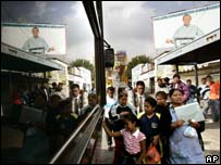 Pessoas em ponto de ônibus na Cidade do México, à frente de cartaz de campanha