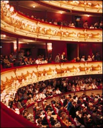 O interior iluminado da Royal Opera House com o público na platéia