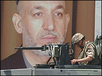 سرباز آيساف، در برابر عکس حامد کرزی در کابل