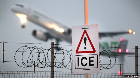 An ice warning sign at Heathrow airport as a plane takes off behind