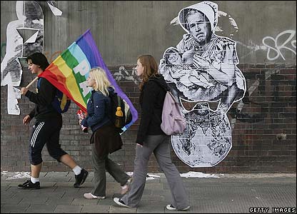 Những người biểu tình đi ngang qua biếm họa vẽ ông Bush bế thủ tướng Đức Angela Merkel