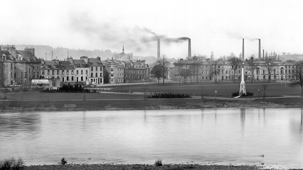 Black and white view across the River Tay to Perth's North Inch, with industrial chimneys behind.