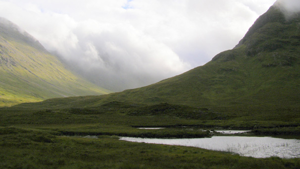 A view of glencoe with a loch and clouds in the distance