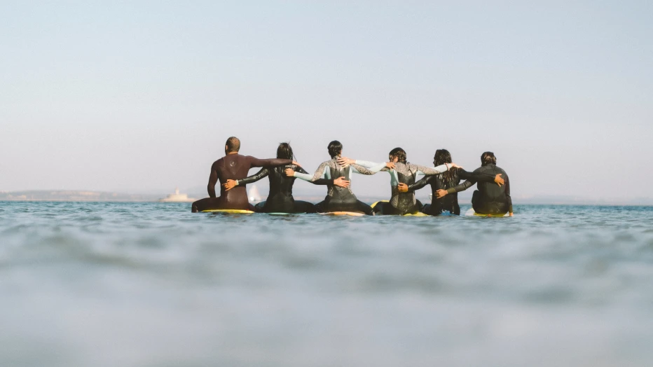 Group sat on surfboards looking out to sea with their arms around each other.